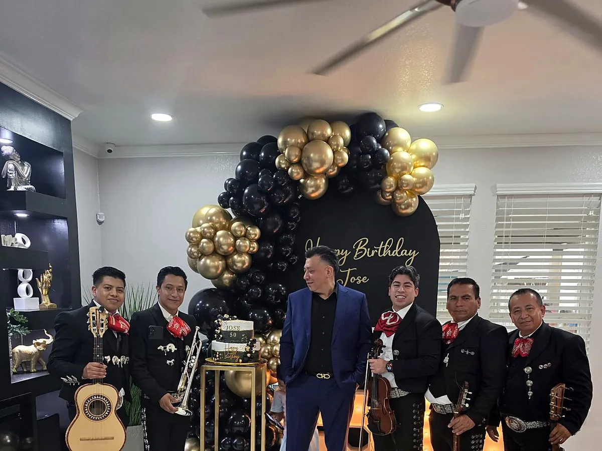 El grupo junto al festejado ante un arco de globos negros y dorados de cumpleaños
