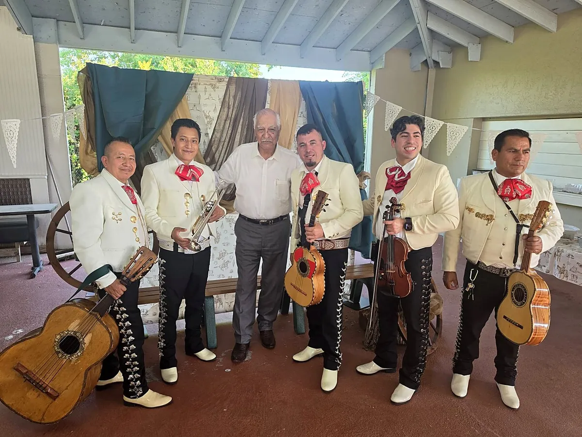 Los músicos con traje de charro blanco y botines, con guitarrón, trompeta y violín, en un patio