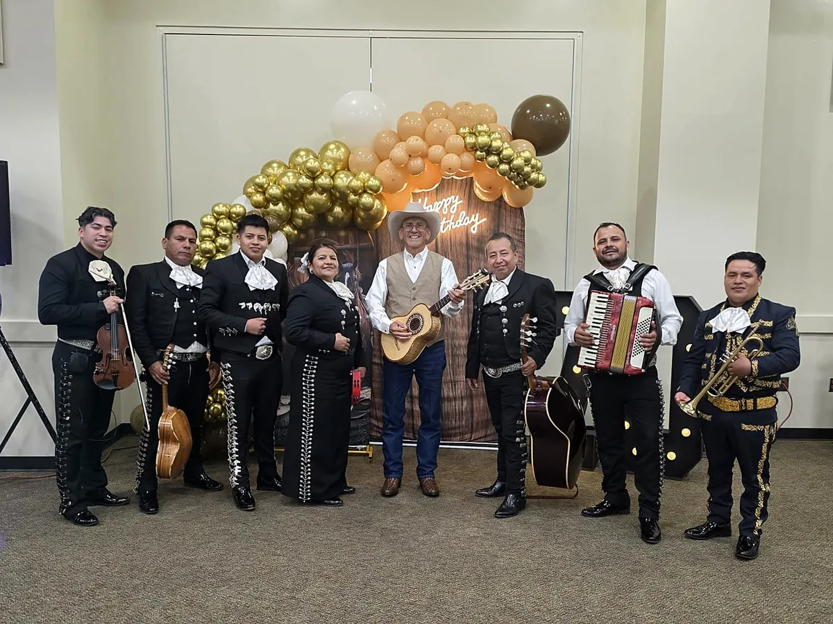 El grupo completo con acordeón y guitarrón ante un arco de globos dorados