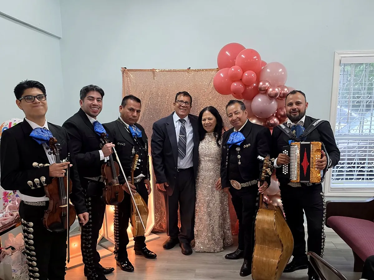 Los músicos junto a una pareja y su familia ante un arco de globos rojos